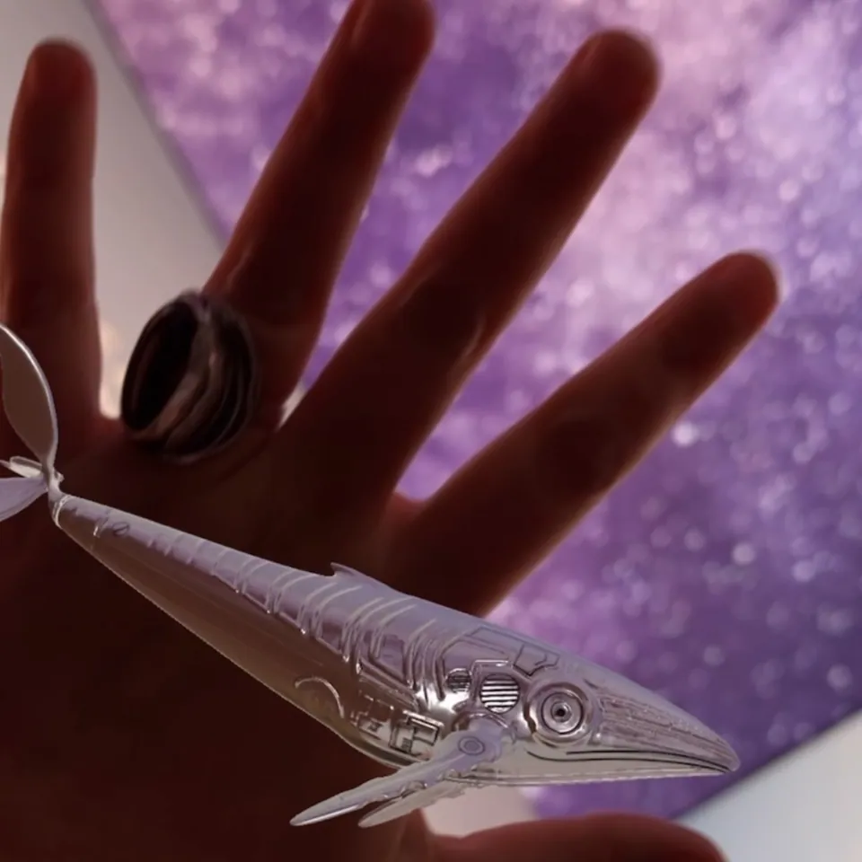 A hand holds a silver hummingbird figure against a violet sky.