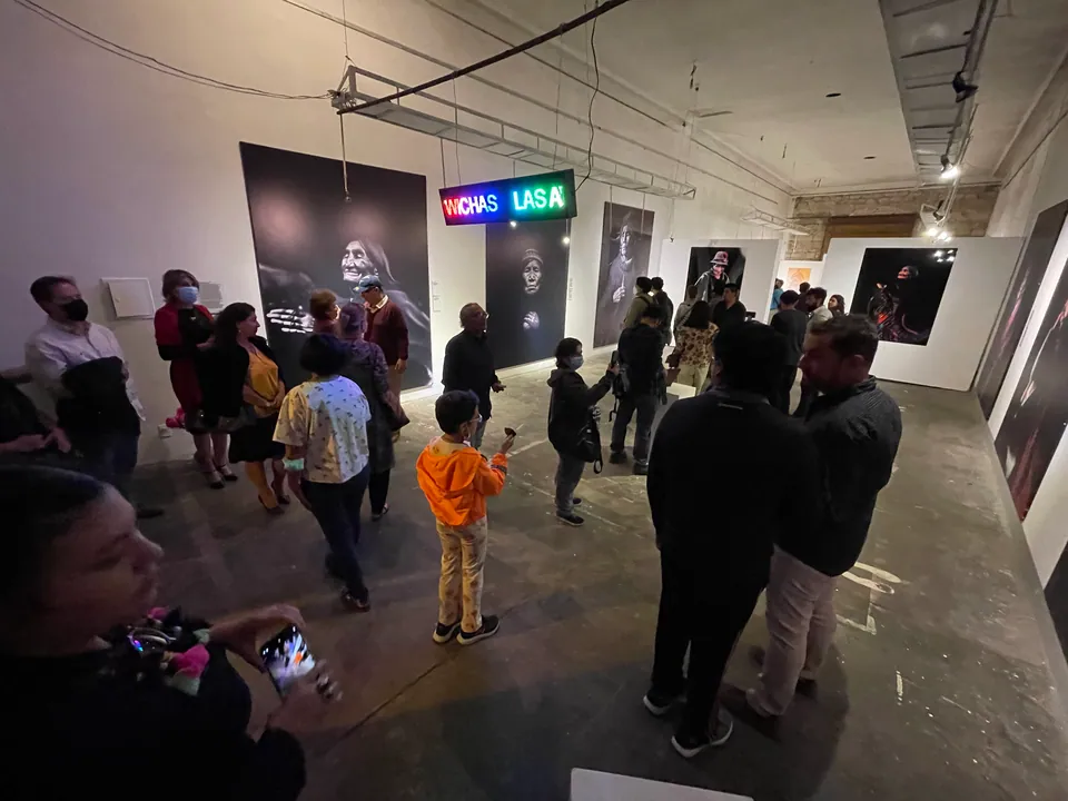 Visitors fill a gallery hung with large black and white portraits, under a light sign reading Las Awichas.