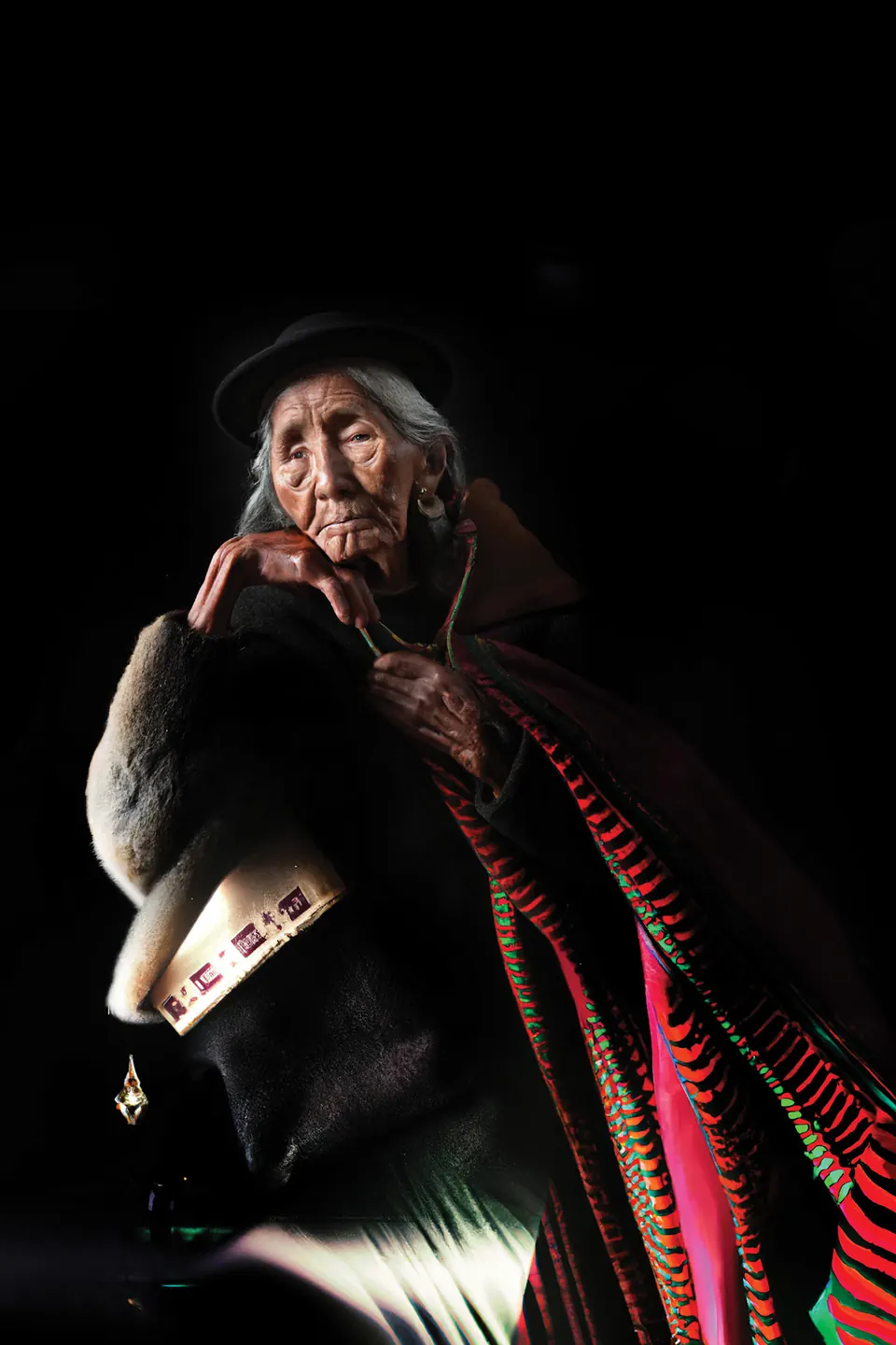 A grandmother in a small black hat, wrapped in layers of fur and red and pink striped cloth.