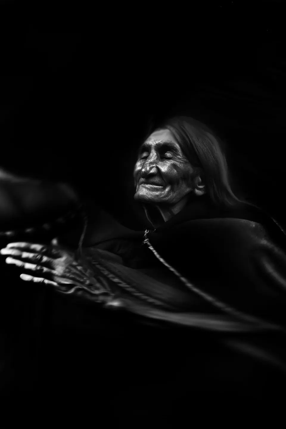 In the dark, a smiling grandmother reaches out a hand that blurs with movement.