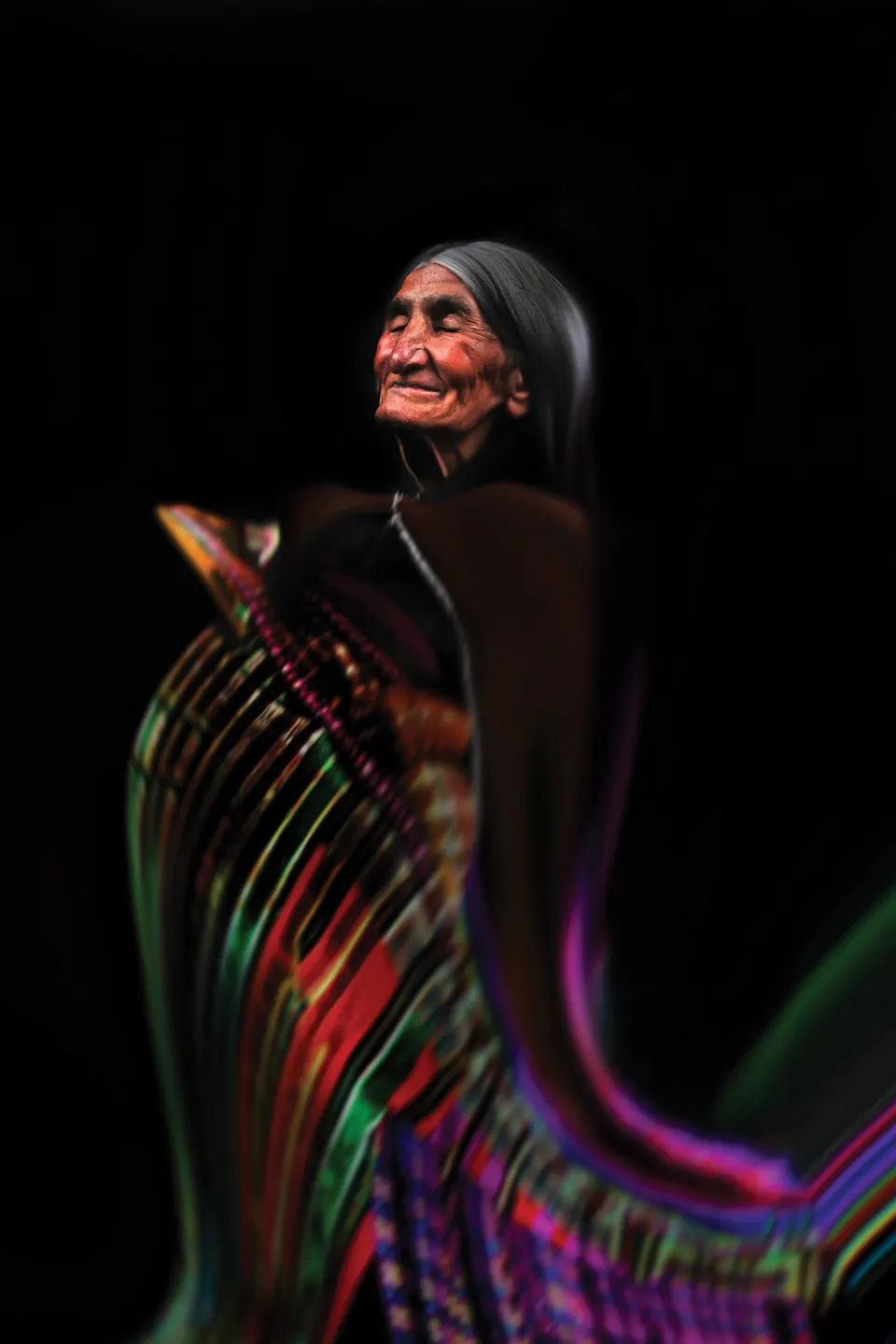 A grandmother lit in red turns her head, her skirt swirling in streaks of green, pink and purple.