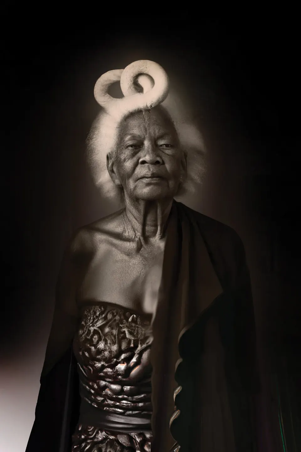 A grandmother with white hair coiled in loops above her head wears a dark shawl over a metallic dress.