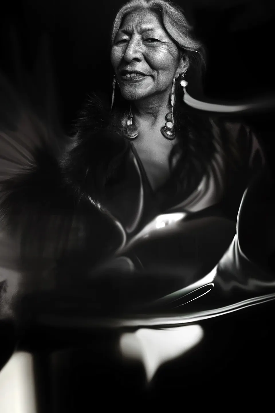 In black and white, a smiling grandmother with long earrings, her shawl melting into light.