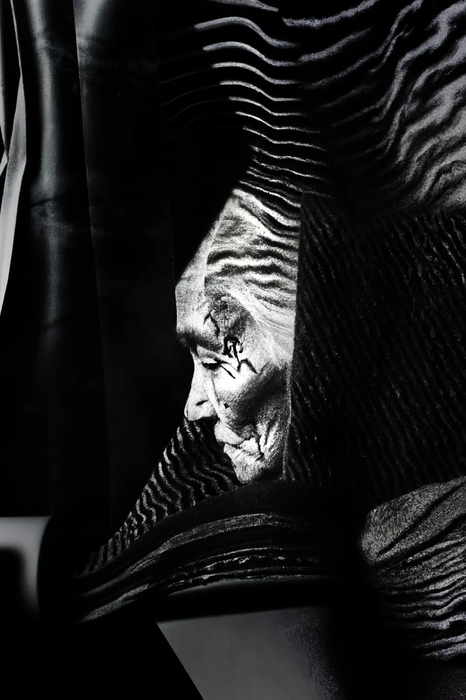 In black and white, the face of a grandmother in profile behind sheets of rippled cloth.