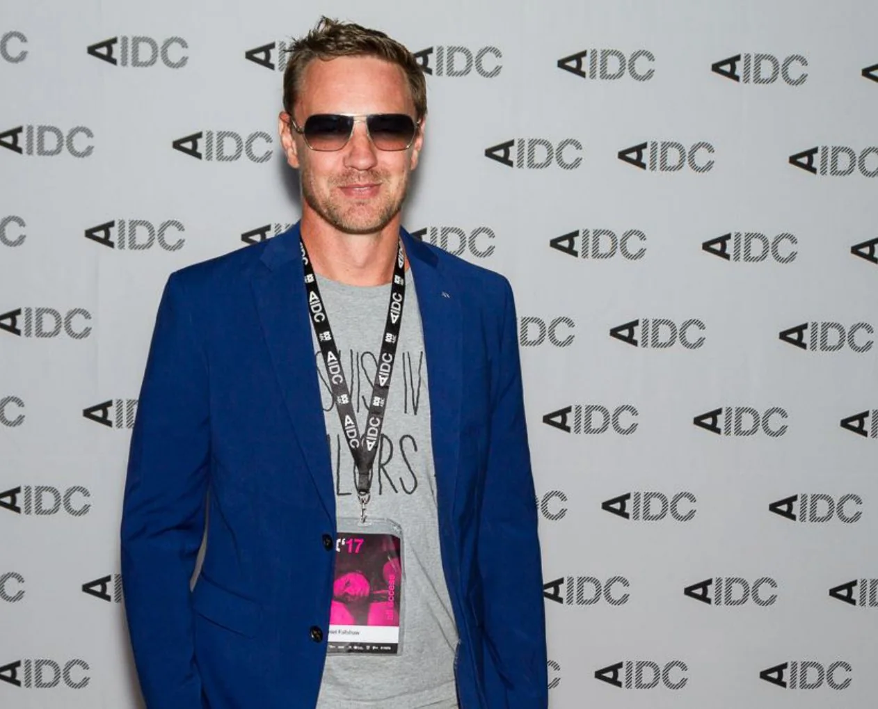 Un hombre con lentes de sol y chaqueta azul, de pie frente a un fondo de AIDC.