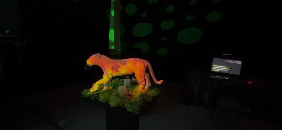 Una escultura de jaguar blanco sobre un pedestal de musgo brilla con luz naranja proyectada. Manchas de luz verde cubren la pared de atrás.
