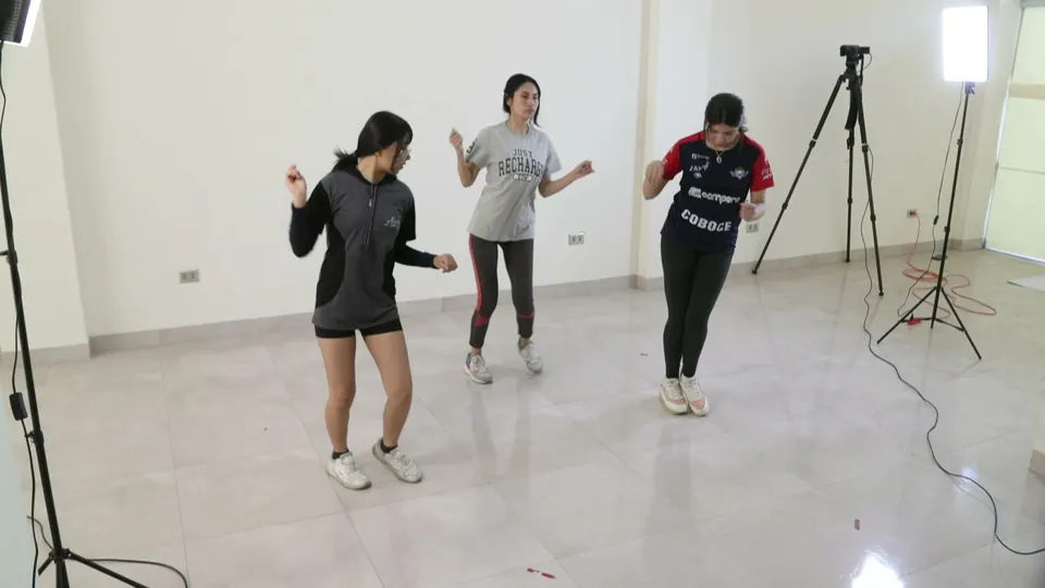 Tres bailarinas bailan kullawada juntas en una sala blanca con trípodes y luces.