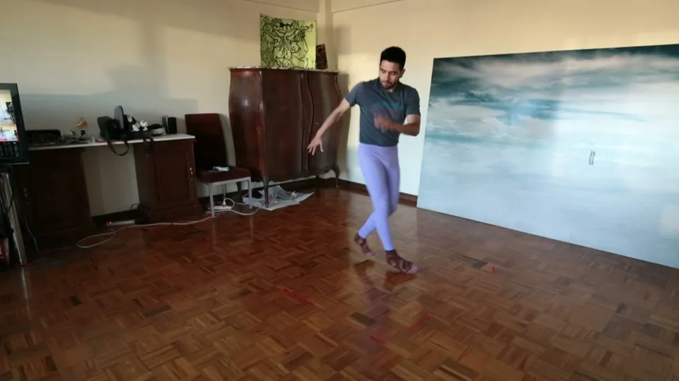 Un bailarín se mueve sobre un piso de parquet, junto a muebles antiguos y un cuadro grande.