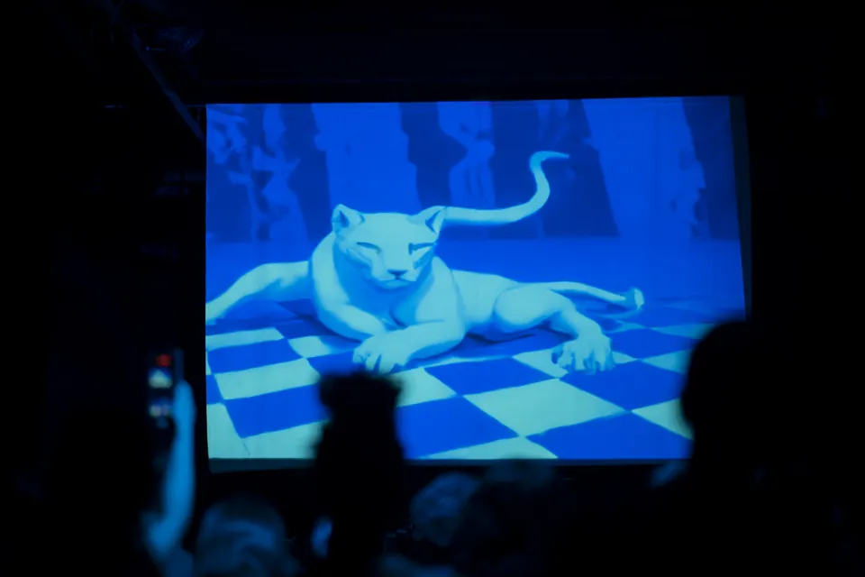 Una pantalla muestra un jaguar blanco generado, echado sobre un piso a cuadros, sobre las siluetas del público.