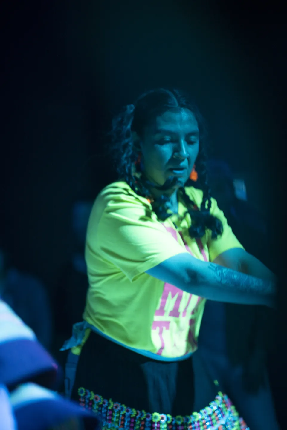 Una bailarina con polera amarillo fuerte y pollera con mostacillas se mueve bajo luz azul.