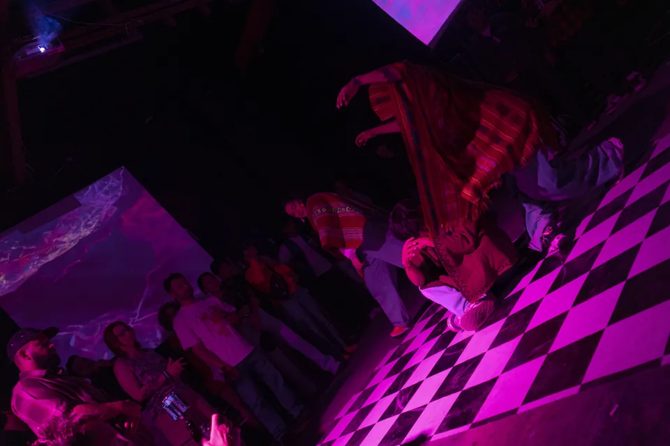 Bailarines sobre un piso a cuadros magenta, el público muy cerca.