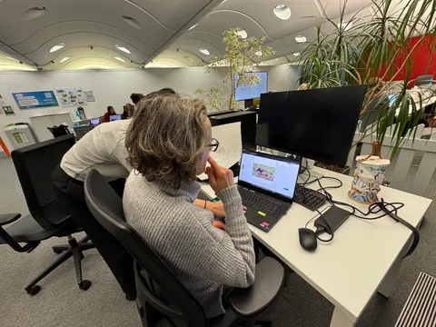 A person works on a laptop in an open office with plants.