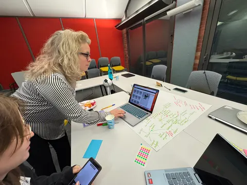 A person leans over a table with a laptop and a large sheet of handwritten notes.