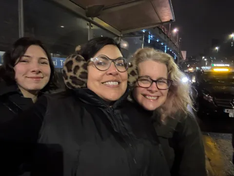 Three people smile close to the camera, in the street at night.